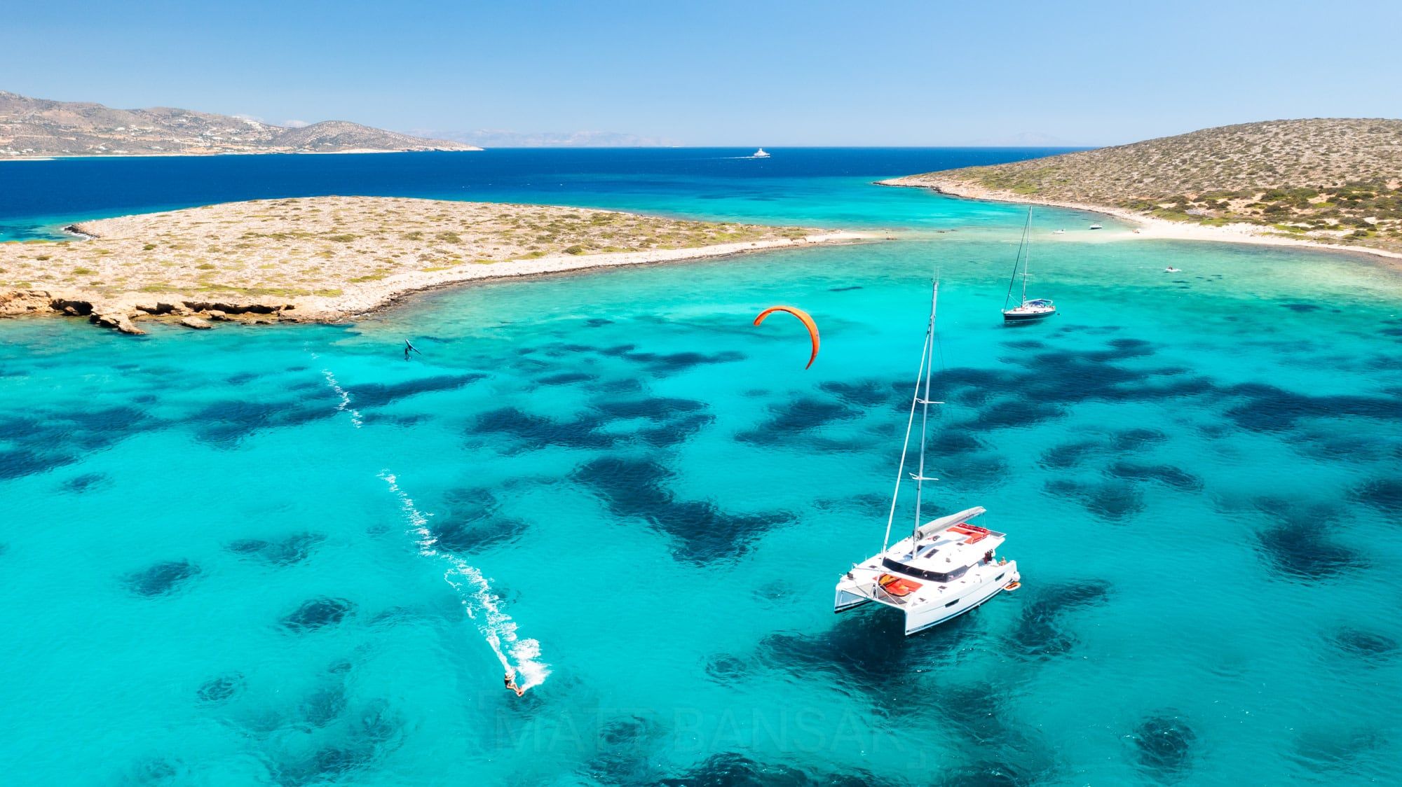 Aerial of a catamaran and kiteboarders in turquoise water