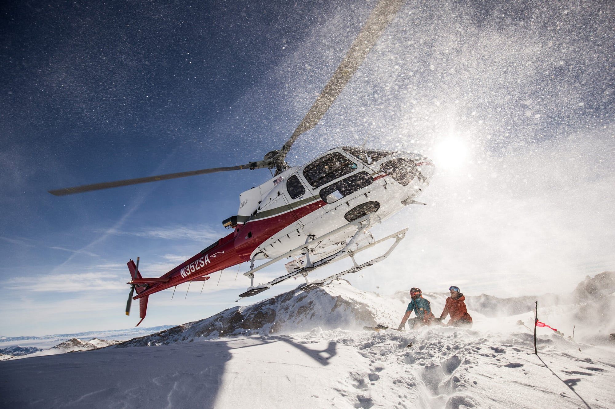 Helicopter landing in swirling snow beside skiers, Ruby Mountains