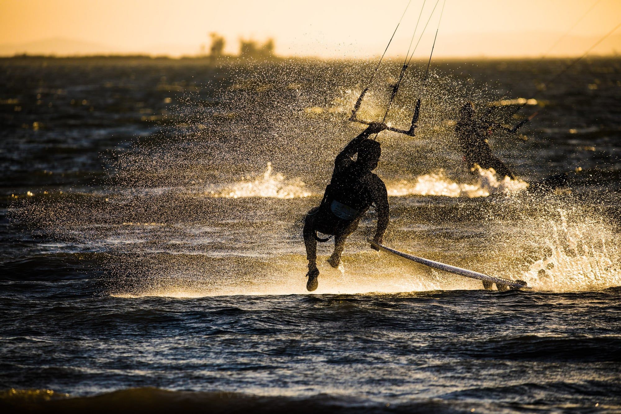 Kiteboarder silhouetted in golden spray at sunset